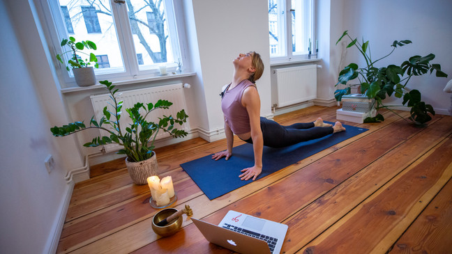 FILE – A woman warms up before an online workout stream session in her home.{&nbsp;}Yoga - which blends movements and poses with deep breathing, meditation, and stretching - has many potential health and physical benefits that can help you fight back against chronic pain. (Photo by Maja Hitij/Getty Images)