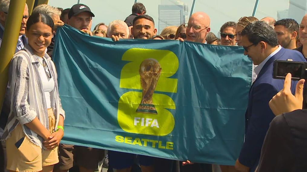 Seattle Sounders star{&nbsp;}Cristian Roldan holds up the new Seattle FIFA World Cup 2026 logo flag at the Space Needle on May 18, 2023, joined by Mayor Bruce Harrell, Washington Gov. Jay Inslee and more. (KOMO News)