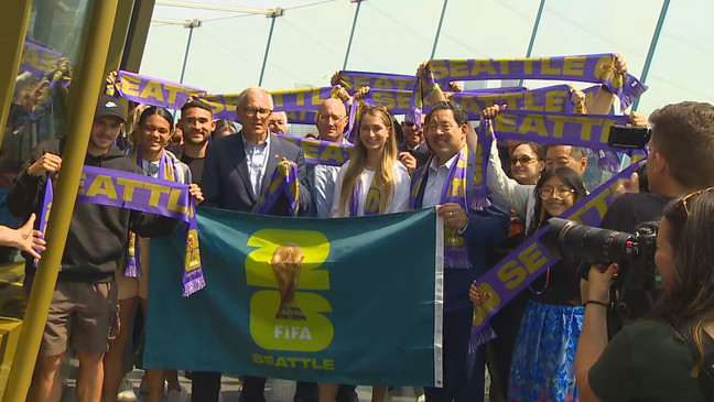 Seattle Sounders star{&nbsp;}Cristian Roldan holds up the new Seattle FIFA World Cup 2026 logo flag at the Space Needle on May 18, 2023, joined by Mayor Bruce Harrell, Washington Gov. Jay Inslee and more. (KOMO News)