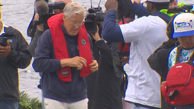 Seahawks head coach Pete Carroll puts on a lifejacket before going out on Lake Washington in a canoe with the team’s rookies. (KOMO News)